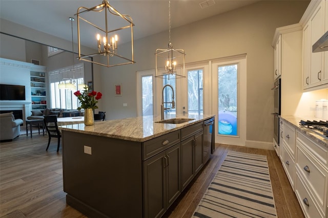 kitchen featuring white cabinetry, dark brown cabinets, decorative light fixtures, sink, and a center island with sink