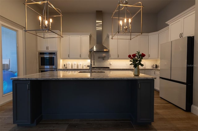 kitchen featuring white cabinetry, wall chimney range hood, white refrigerator, and a center island with sink