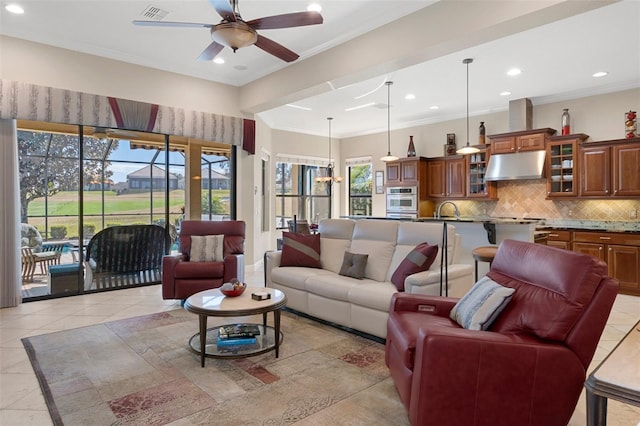 tiled living room featuring crown molding, sink, and ceiling fan with notable chandelier