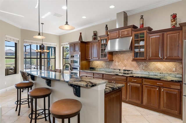 kitchen with decorative light fixtures, tasteful backsplash, a kitchen bar, dark stone counters, and a kitchen island with sink