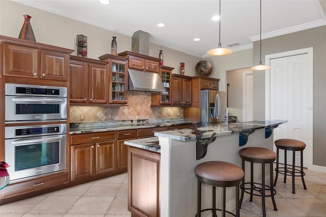 kitchen featuring appliances with stainless steel finishes, a kitchen island with sink, a kitchen breakfast bar, decorative light fixtures, and dark stone counters