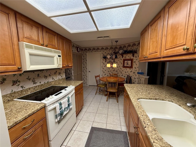 kitchen with sink, white appliances, light tile patterned floors, hanging light fixtures, and light stone countertops