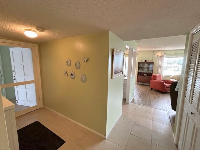 hallway with a textured ceiling and light tile patterned floors