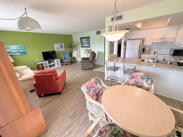 dining space featuring light hardwood / wood-style floors, sink, and a textured ceiling