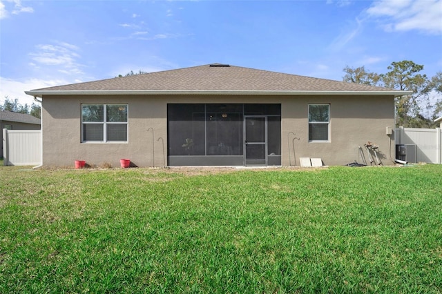 rear view of property featuring a shingled roof, a lawn, a sunroom, fence, and stucco siding