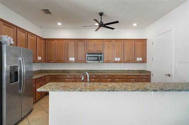 kitchen with stone counters, visible vents, appliances with stainless steel finishes, brown cabinetry, and light tile patterned flooring