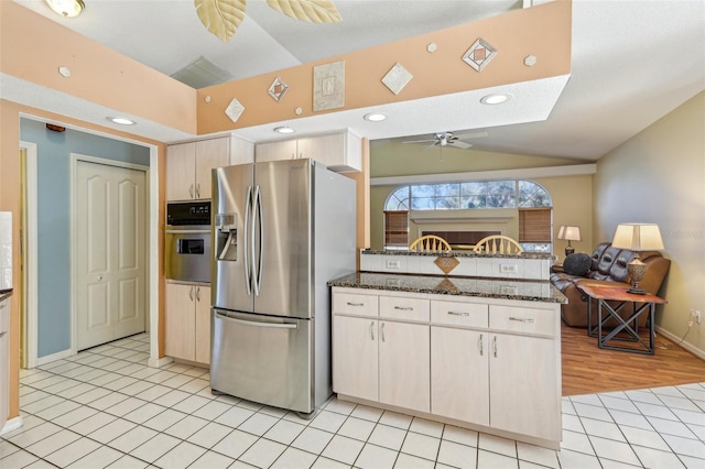 kitchen featuring ceiling fan, appliances with stainless steel finishes, dark stone counters, and lofted ceiling