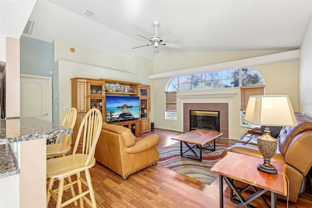 living room with ceiling fan, lofted ceiling, a fireplace, and light hardwood / wood-style flooring