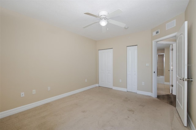 unfurnished bedroom featuring ceiling fan, light carpet, and two closets