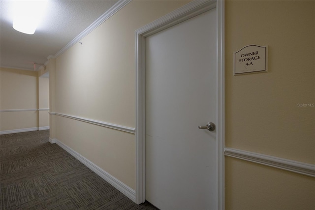 hallway featuring a textured ceiling, ornamental molding, and dark colored carpet