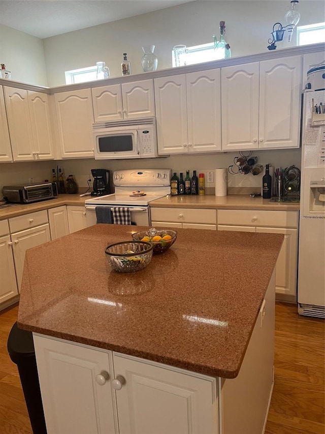 kitchen with a center island, wood-type flooring, white appliances, white cabinetry, and dark stone counters