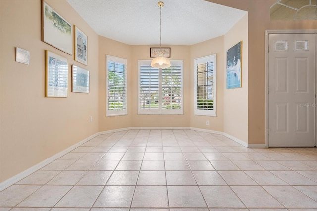 unfurnished dining area with light tile patterned floors, a textured ceiling, and baseboards