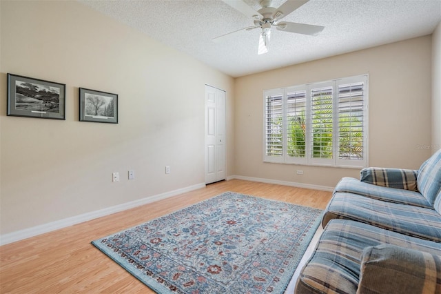 living area featuring a textured ceiling, light wood finished floors, and baseboards