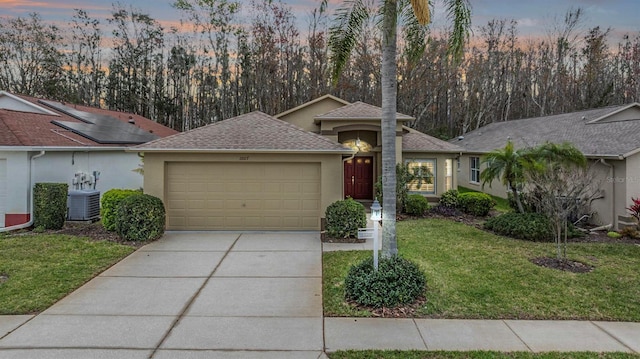 ranch-style house with a garage, driveway, central AC unit, a lawn, and stucco siding