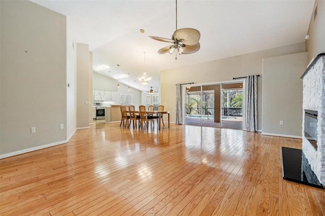 unfurnished living room with high vaulted ceiling, light wood-style flooring, ceiling fan with notable chandelier, a fireplace, and baseboards