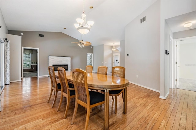 dining space with visible vents, lofted ceiling, light wood-style floors, and a glass covered fireplace