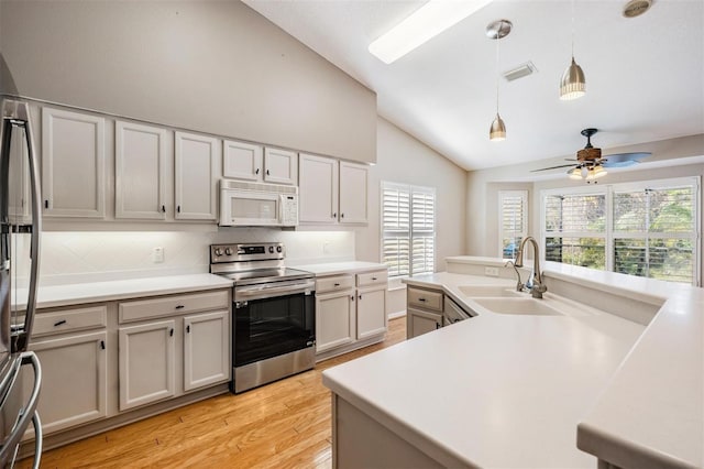 kitchen featuring pendant lighting, a sink, appliances with stainless steel finishes, light countertops, and vaulted ceiling