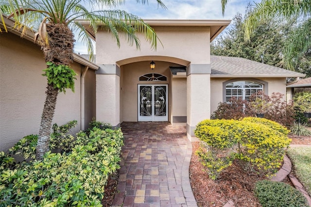 entrance to property with stucco siding, french doors, and a shingled roof