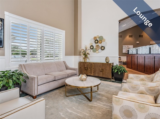 living area with a wainscoted wall, high vaulted ceiling, and visible vents