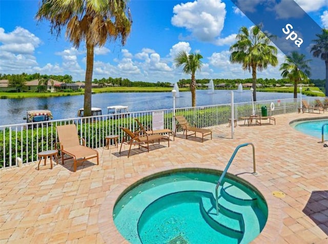 view of pool with a hot tub, fence, a patio, and a water view