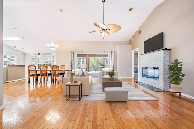 living area featuring visible vents, high vaulted ceiling, a stone fireplace, light wood finished floors, and baseboards