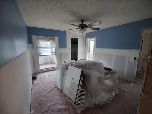 interior space featuring ceiling fan, multiple windows, and a textured ceiling