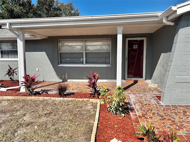 doorway to property featuring a porch, concrete block siding, and stucco siding