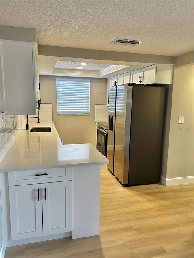 kitchen with a tray ceiling, stainless steel appliances, visible vents, a sink, and light wood-type flooring