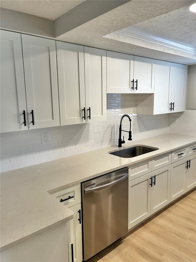 kitchen with a sink, light wood-style flooring, stainless steel dishwasher, and a textured ceiling