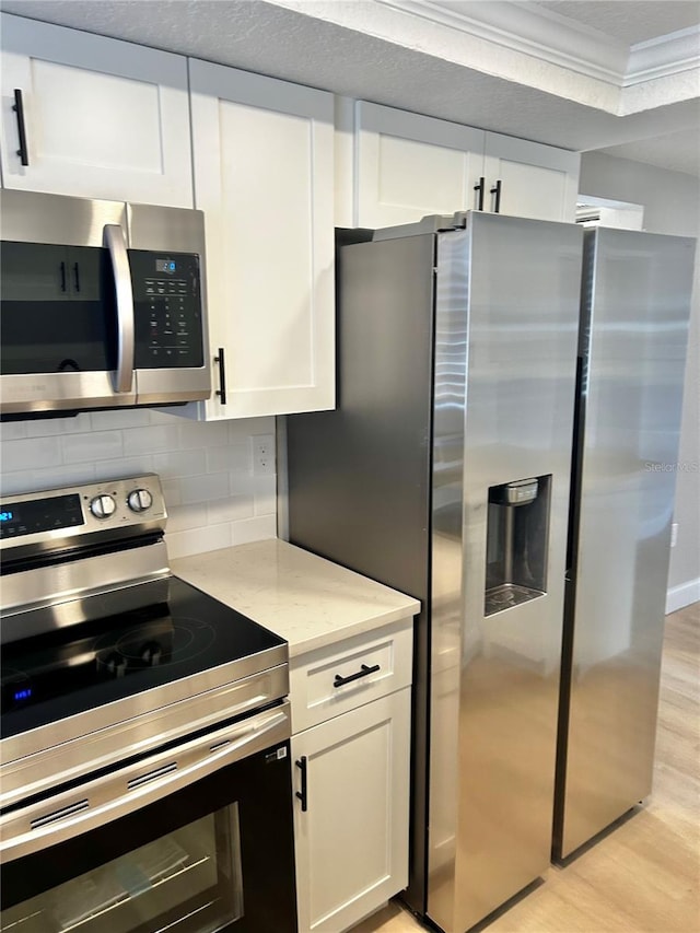 kitchen with stainless steel appliances, white cabinetry, light wood-type flooring, backsplash, and crown molding