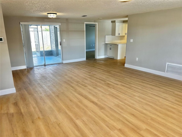 unfurnished living room featuring visible vents, light wood-style flooring, baseboards, and a textured ceiling