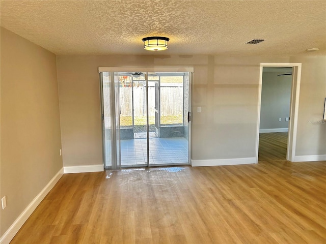 empty room featuring a textured ceiling, wood finished floors, visible vents, and baseboards