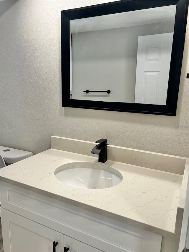 bathroom with a textured wall, vanity, and toilet