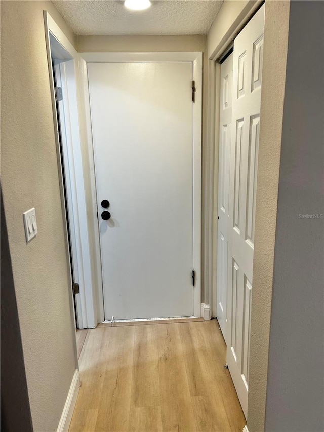 corridor featuring a textured ceiling, a textured wall, and light wood-style flooring