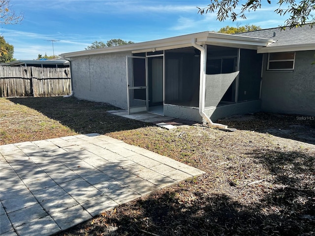 back of house featuring a sunroom, a patio area, fence, and stucco siding