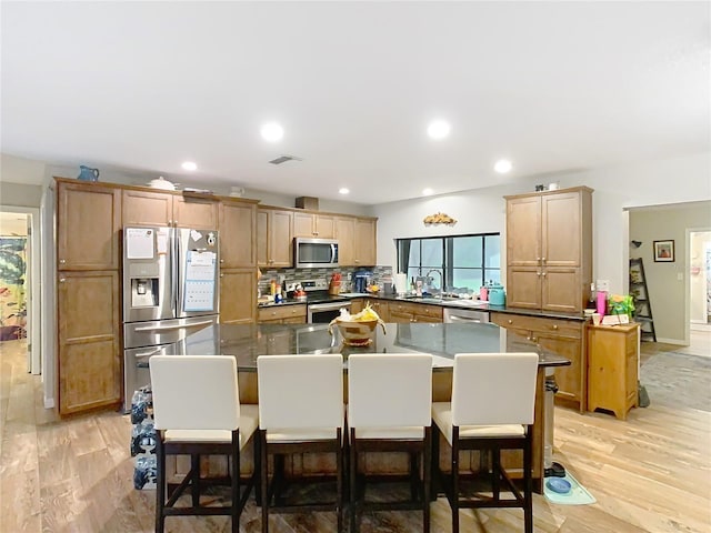 kitchen with light hardwood / wood-style floors, backsplash, a kitchen bar, and appliances with stainless steel finishes