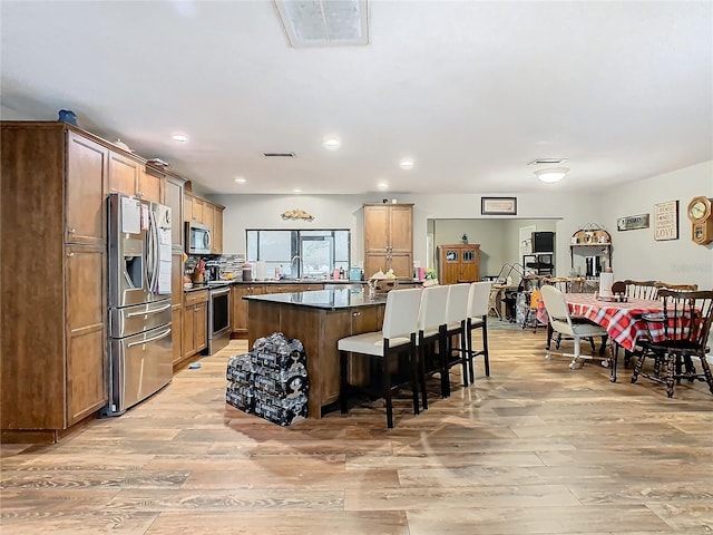 kitchen with a center island, stainless steel appliances, tasteful backsplash, light hardwood / wood-style floors, and a breakfast bar area