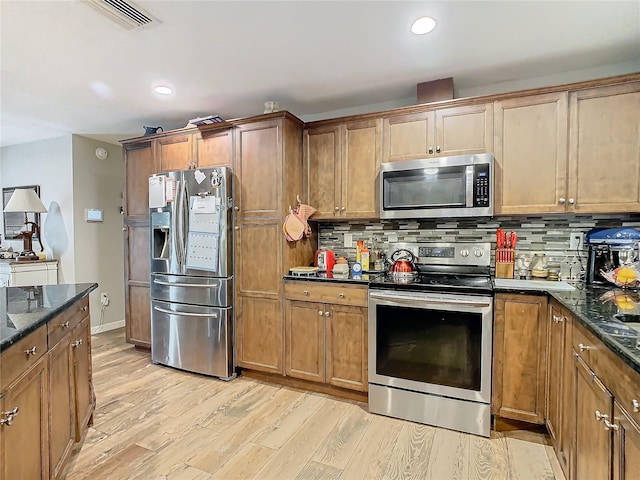 kitchen featuring light hardwood / wood-style floors, tasteful backsplash, dark stone countertops, and appliances with stainless steel finishes