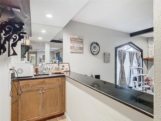 kitchen featuring sink, kitchen peninsula, beam ceiling, and dark stone counters