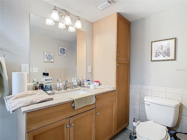 bathroom with toilet, vanity, tile patterned floors, and tile walls