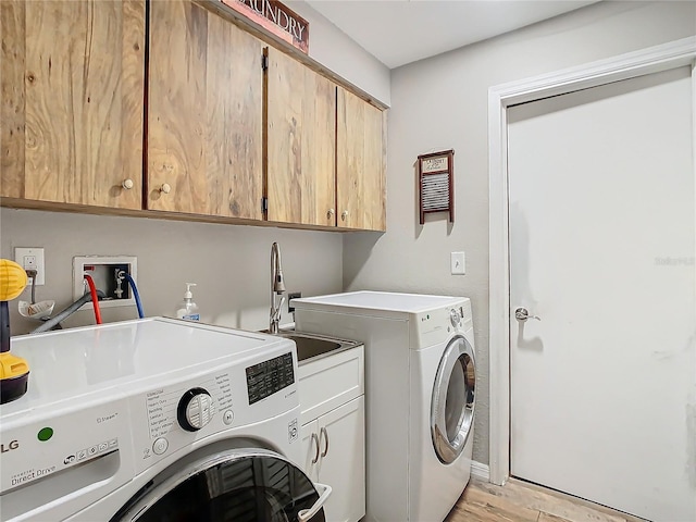 laundry area featuring sink, washer and clothes dryer, light hardwood / wood-style floors, and cabinets