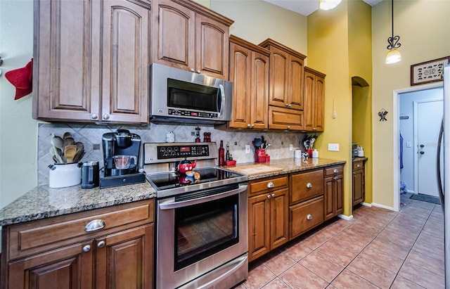 kitchen featuring tasteful backsplash, light stone countertops, light tile patterned flooring, and appliances with stainless steel finishes