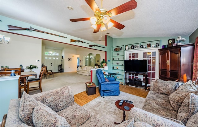 living room featuring ceiling fan with notable chandelier, vaulted ceiling, a textured ceiling, and light wood-type flooring