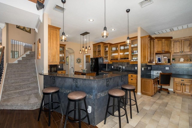 kitchen with pendant lighting, black refrigerator with ice dispenser, decorative backsplash, kitchen peninsula, and a breakfast bar area