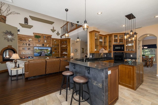 kitchen featuring pendant lighting, black appliances, light hardwood / wood-style floors, kitchen peninsula, and a breakfast bar