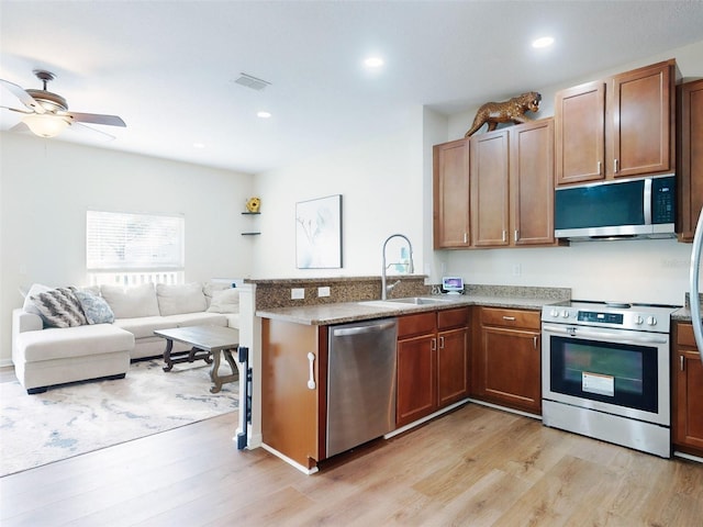 kitchen featuring sink, stone countertops, appliances with stainless steel finishes, kitchen peninsula, and light hardwood / wood-style floors