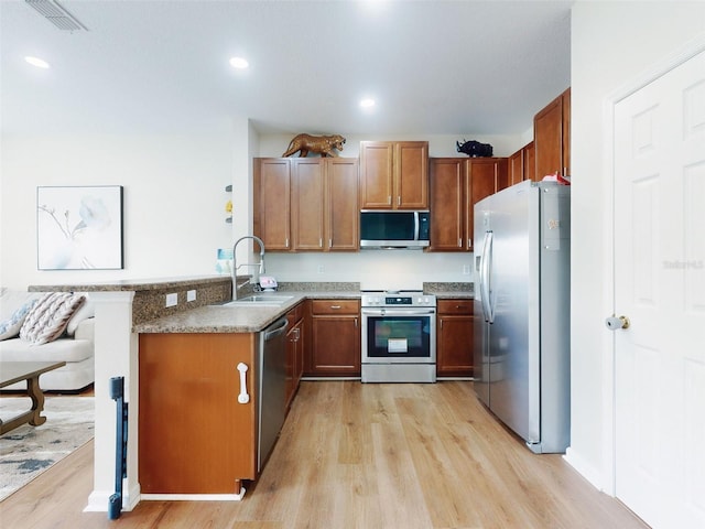 kitchen featuring appliances with stainless steel finishes, sink, kitchen peninsula, light stone countertops, and light wood-type flooring