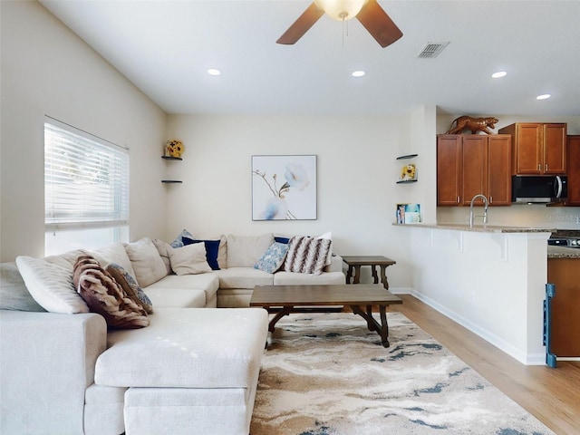 living room with ceiling fan, sink, and light hardwood / wood-style floors