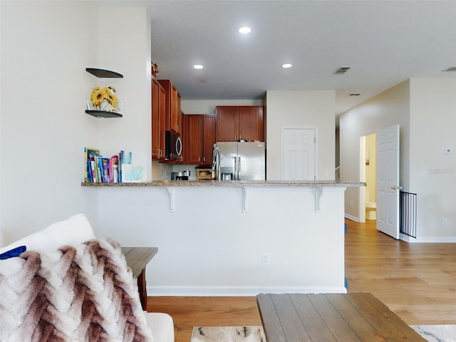 kitchen featuring stainless steel appliances, a kitchen breakfast bar, kitchen peninsula, and light hardwood / wood-style flooring