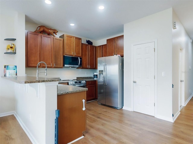 kitchen featuring appliances with stainless steel finishes, dark stone countertops, a kitchen breakfast bar, light hardwood / wood-style floors, and kitchen peninsula